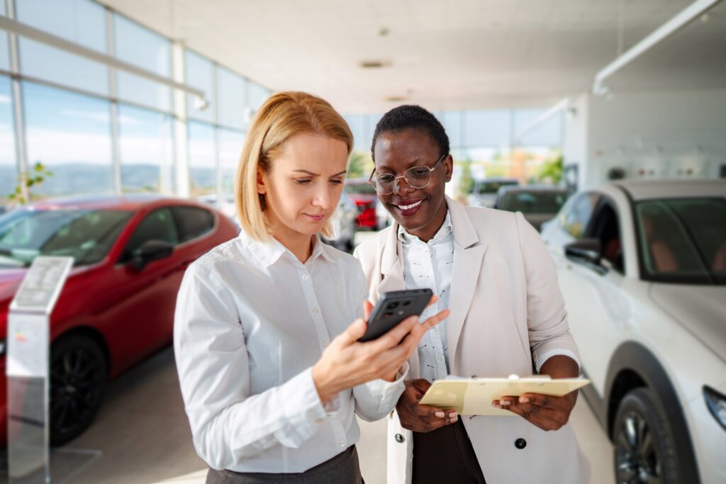 Two automotive professionals reviewing data on a phone in a modern car dealership